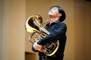 a young male student wearing black dress clothes, embracing his euphonium