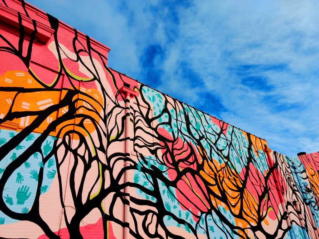 abstract mural on the side of the building. The art includes images that look like tree branches on a colorful background. The sky is visible.