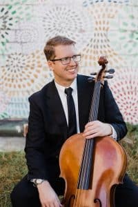 Karl Ronnevik posing with his cello wearing a suit.
