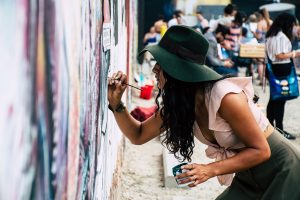 woman wearing green sun hat painting on an outdoor wall
