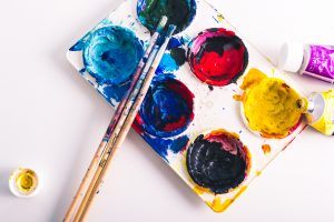 a used paint pallet with three paint brushes and two tubes of paint.